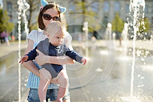 Cute big sister holding her baby brother by city fountain. Adorable teenage girl playing with her baby boy brother. Children