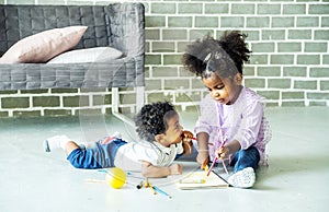 Cute black african american little girl and boy drawing book on floor indoors,  African people - Children
