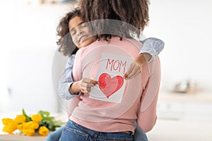 Cute black daughter greeting mom with tulips and card