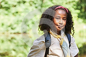 Cute black girl as girl scout looking at camera outdoors in forest