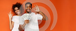Cute black guy and girl holding money fan and gesturing ok