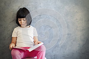 Cute black hair little girl reading book by the wall