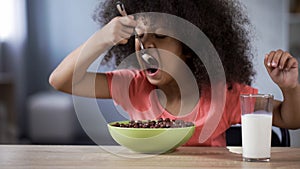 Cute black-haired curly girl eating chocolate cornflakes, unhealthy sugary food