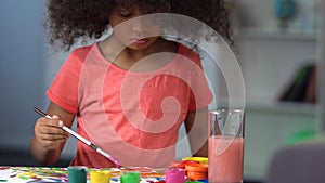 Cute black-haired curly girl painting with watercolors at art school, education