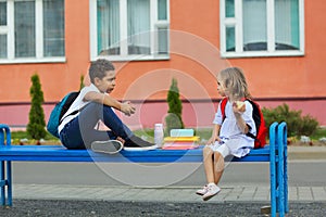 Cute Black schoolboy and girl are eating lunch outdoors next the school.