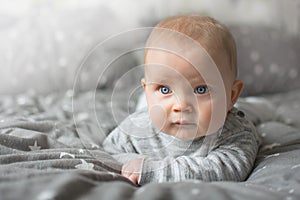 Cute blond baby with blue eyesy is laying on bed