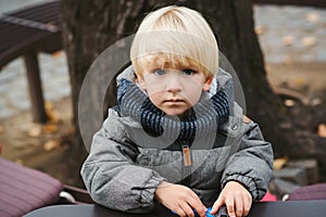 Cute blond baby boy playing with toys outdoors. Toddler boy with blue eyes and blonde hair. Child in warm jacket at walk in cold