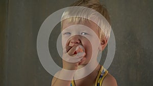 Cute blond baby is eating raw carrots to reinforce his vision. Delicious vegetarian food