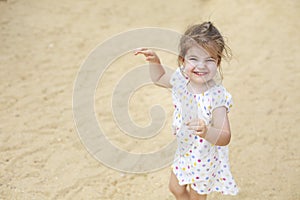 Cute blond baby girl in beautiful dress walking on a long sandy beach