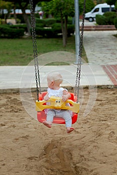 Cute blond baby girl sitting in a swing