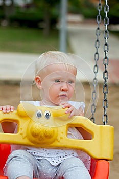 Cute blond baby girl sitting in a swing