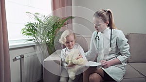 A cute blond baby plays with his favorite toy and talks to a pediatrician.