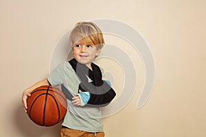 Cute blond boy with broken hand holding basketball ball