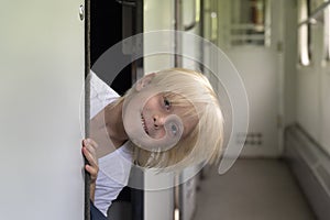 Cute blond boy looks out of compartment in railway carriage. Traveling with children