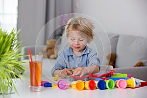 Cute blond child, boy, playing with play doh modeline at home, making different objects