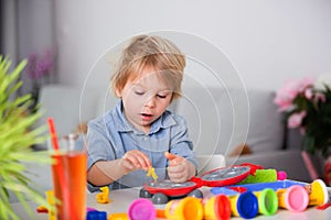 Cute blond child, boy, playing with play doh modeline at home, making different objects