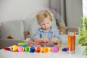 Cute blond child, boy, playing with play doh modeline at home, making different objects