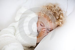 Cute blond curly little boy sleeping on white couch