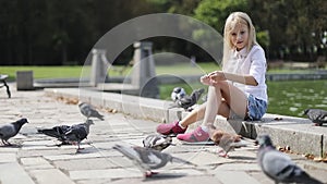 Cute blond girl feeds pigeons with bread in the park.