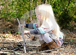 Cute Blond Girl Playing with Twigs on Ground