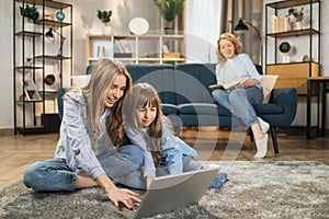 Cute blond girls sisters sitting on warm floor play at home together using laptop