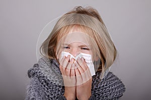 Cute blond hair little girl blowing her nose with paper tissue. Child winter flu allergy health care concept