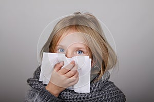 Cute blond hair little girl blowing her nose with paper tissue. Child winter flu allergy health care concept
