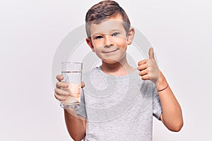 Cute blond kid drinking glass of water smiling happy and positive, thumb up doing excellent and approval sign
