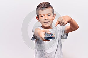 Cute blond kid holding television remote control smiling happy pointing with hand and finger