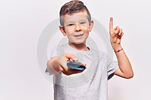 Cute blond kid holding television remote control smiling with an idea or question pointing finger with happy face, number one