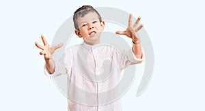 Cute blond kid wearing elegant shirt shouting frustrated with rage, hands trying to strangle, yelling mad