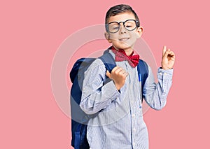 Cute blond kid wearing nerd bow tie and backpack surprised with an idea or question pointing finger with happy face, number one