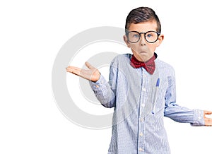 Cute blond kid wearing nerd bow tie and glasses clueless and confused expression with arms and hands raised