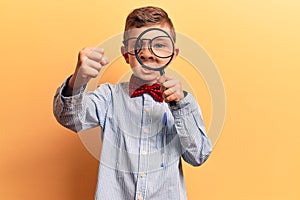 Cute blond kid wearing nerd bow tie and glasses holding magnifying glass annoyed and frustrated shouting with anger, yelling crazy