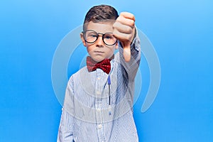 Cute blond kid wearing nerd bow tie and glasses looking unhappy and angry showing rejection and negative with thumbs down gesture