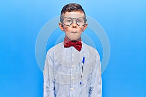 Cute blond kid wearing nerd bow tie and glasses making fish face with lips, crazy and comical gesture