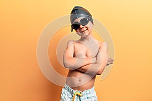 Cute blond kid wearing swimwear and swimmer glasses happy face smiling with crossed arms looking at the camera