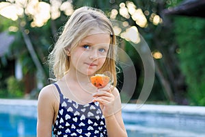 Cute blond little girl in blue swimsuit sitting at the swimming pool, eating passion fruit. Enjoy eating tropical fruit. Summer