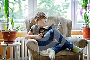 Cute blond little kid boy reading magazine in domestic room.