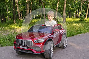 Cute blond little young toddler kid child boy driving,riding in electric toy car,automobile in park.Children physical,emotional