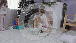 Cute blond sibling sisters are searching for presents under a Christmas tree