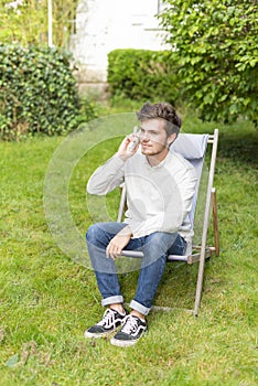 Cute blond teenager on the phone sitting in the garden