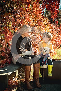 Cute blond Toddler boy talking to young smiling stranger woman sitting on a bench in autumn park. Rules for the behavior