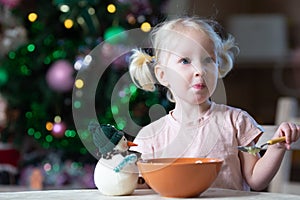 Cute blond toddler girl with blue eyes having her meal in christmas entourage
