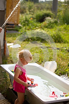 Cute blond toddler girl playing with toys in bathtub outdoors