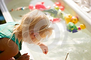 Cute blond toddler girl playing with toys in bathtub outdoors on summer day