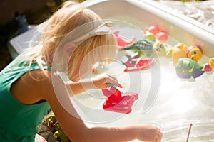 Cute blond toddler girl playing with toys in bathtub outdoors on summer day