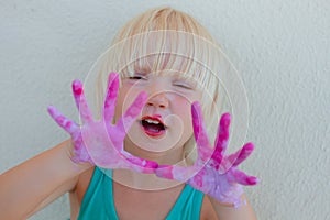 Cute blond toddler girl showing painted pink and violet hands