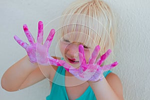 Cute blond toddler girl showing painted pink and violet hands