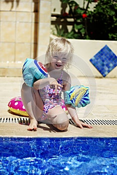 Cute blond toddler girl wearing armbands standing near the pool in a summer day